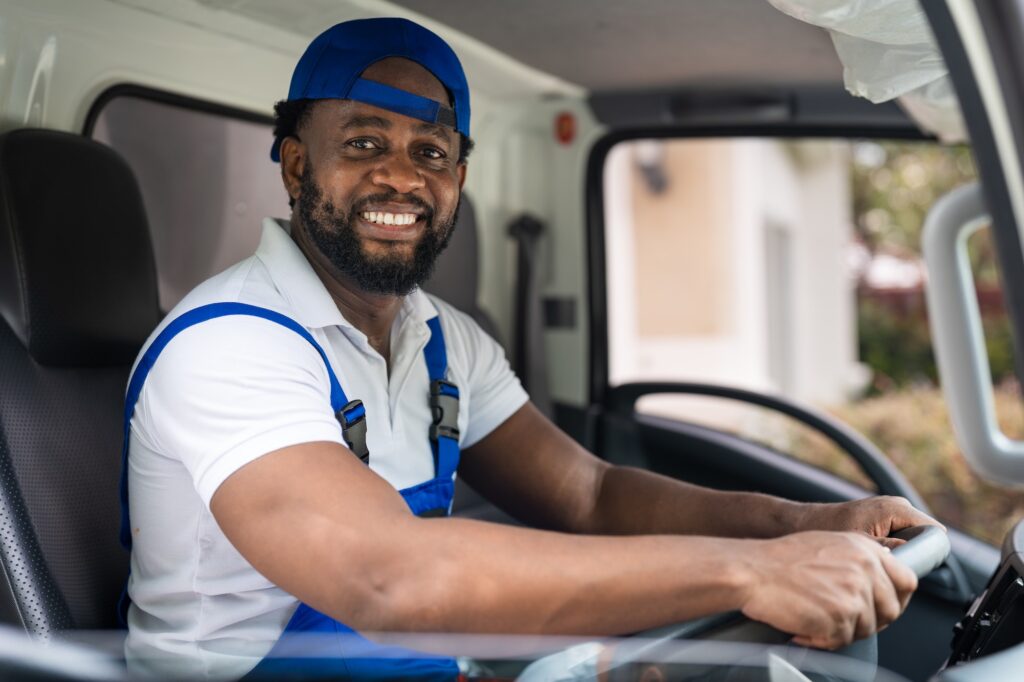 Smiling man mover worker in blue uniform driving truck to delivery and moving house service
